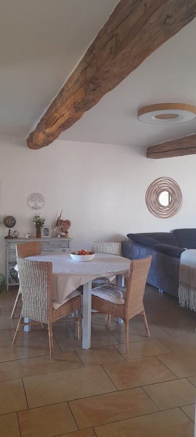 Salle à manger avec une table ronde, chaises en osier et un mur clair.